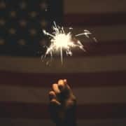 Someone holding a sparkler up to an American flag for 4th of July.