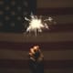 Someone holding a sparkler up to an American flag for 4th of July.