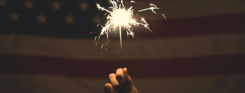 Someone holding a sparkler up to an American flag for 4th of July.