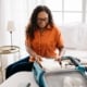 Senior woman smiling as she packs her folded clothing into her blue luggage, while lounging on her bed