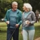 A senior couple in athletic wear walking their dog down a paved brick path, smiling at each other