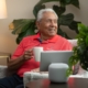 Resident of Heritage Community in Kalamazoo smiling as he drinks a cup of coffee as he sits on a chair