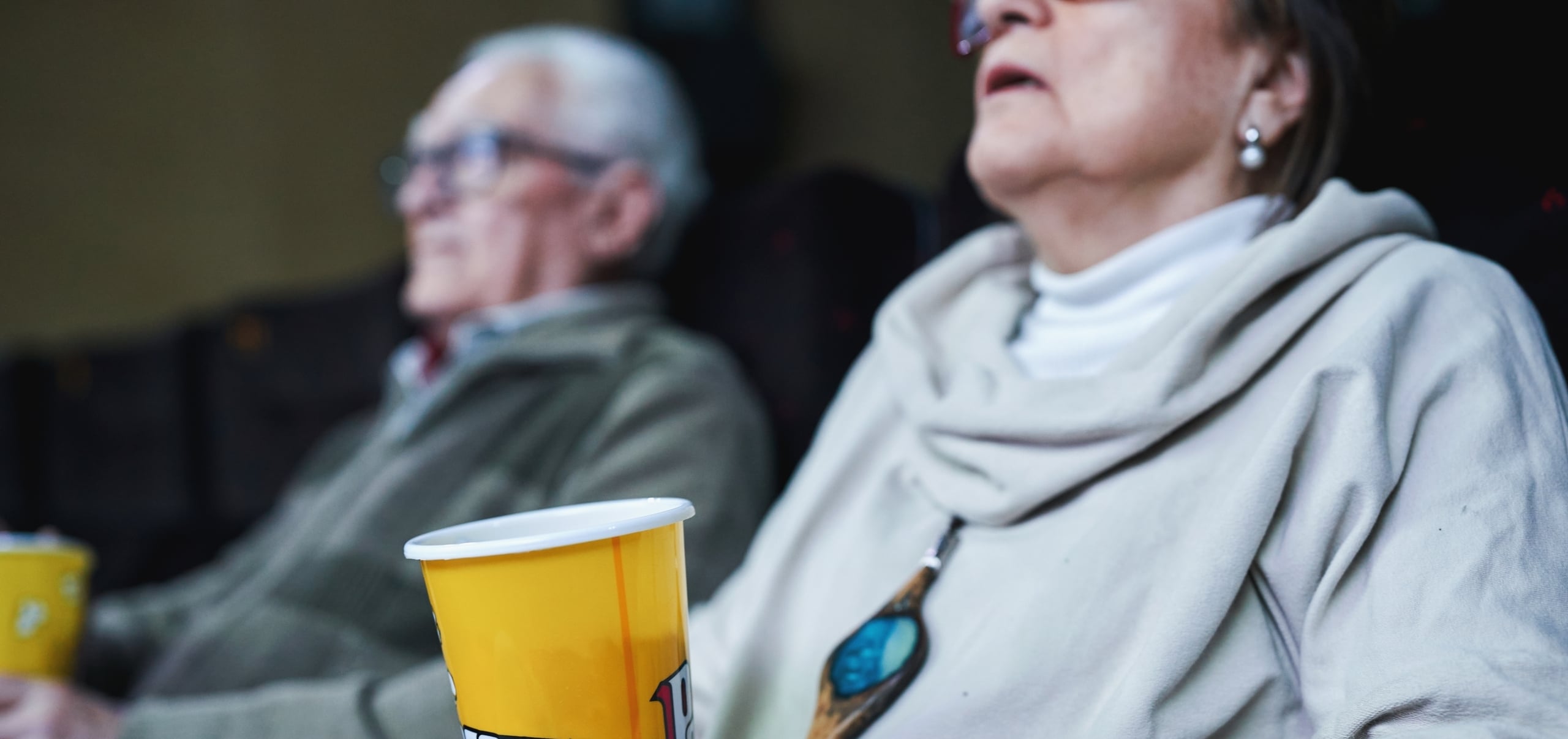 Close up of elderly couple at the movie theater holding popcorn cup.