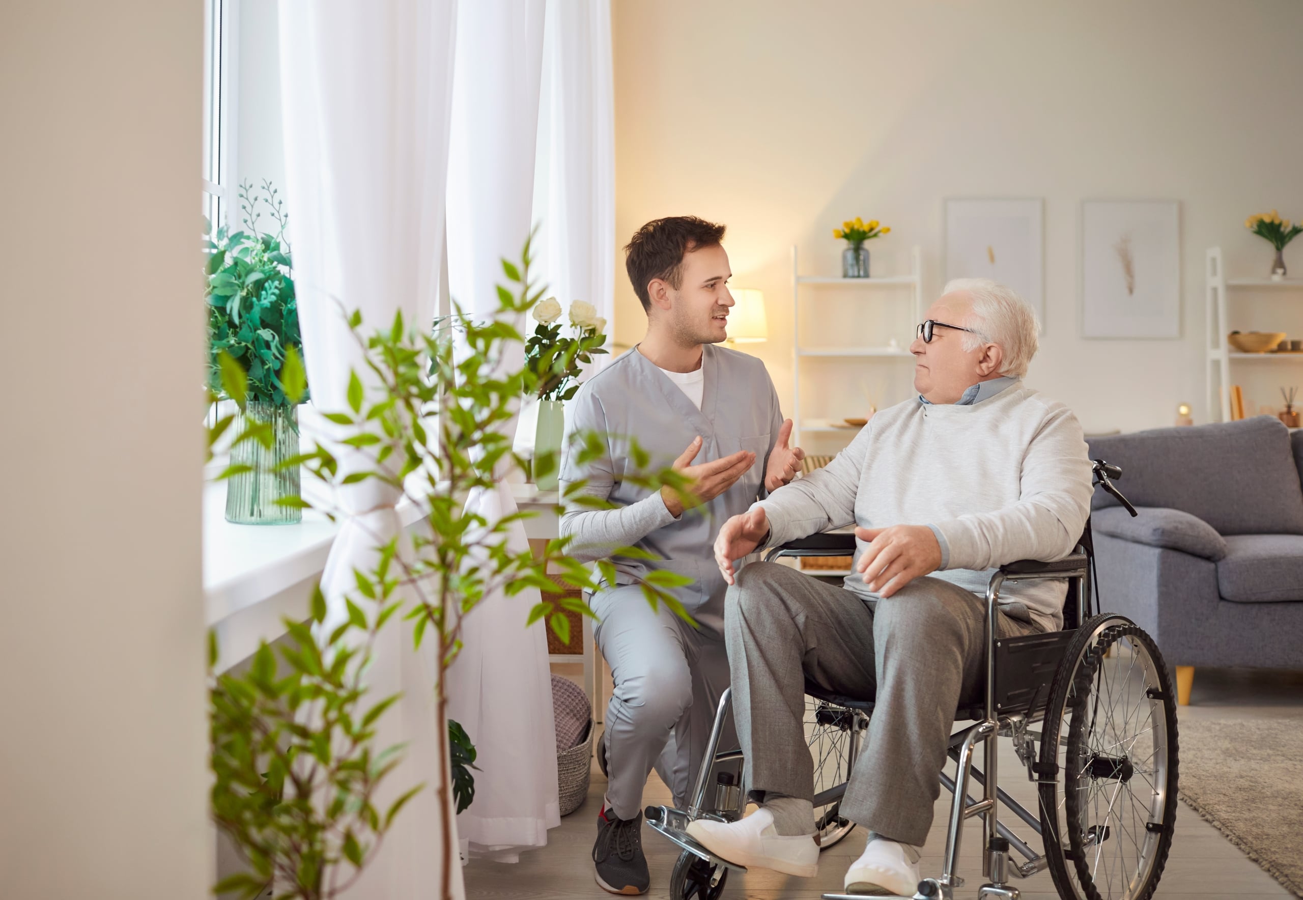 Senior man in wheelchair talking to young man in scrubs.