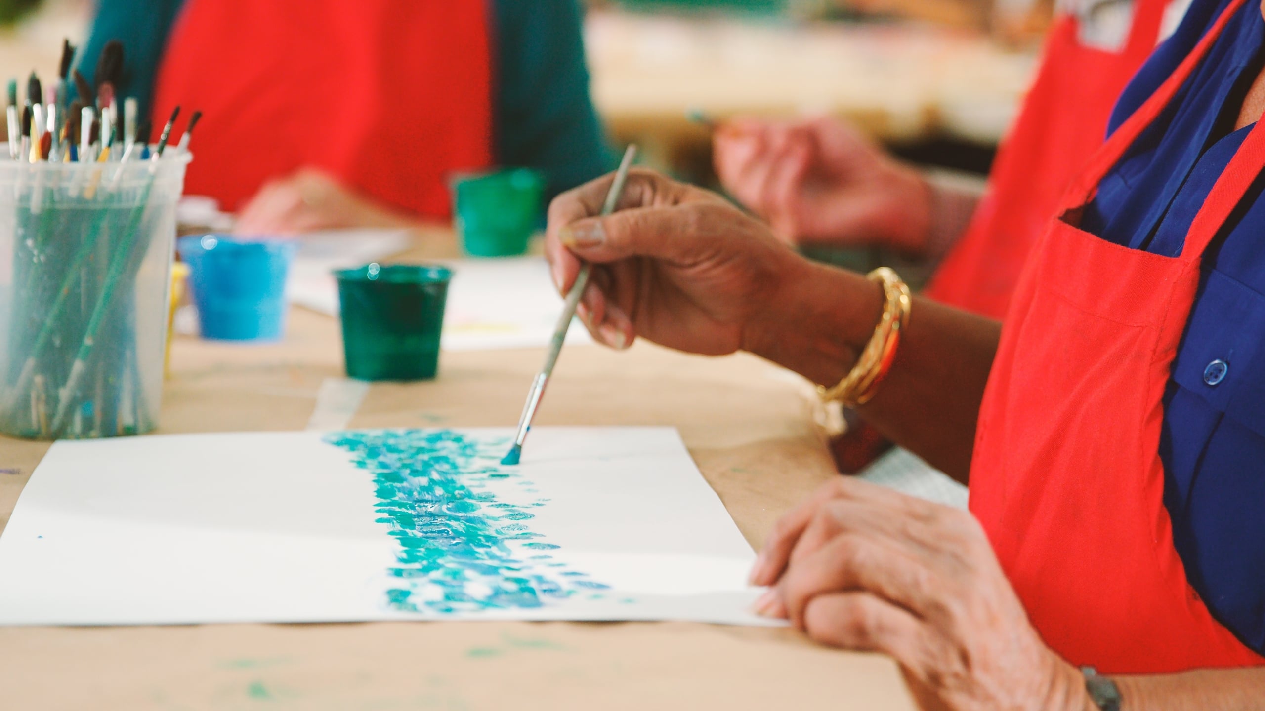 Close up of a woman in an apron painting with a group.
